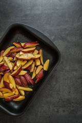 Kartoffelspalten mit Salz, Pfeffer, und Olivenöl in einer Auflaufform auf eine dunklen Hintergrund