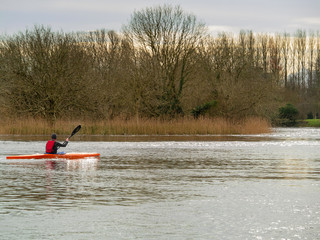 Man in life jacket rowing in a kayak on  a river, Cloudy sky, Selective focus.