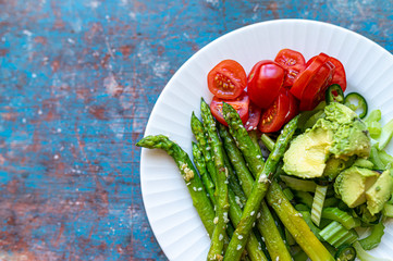 White plate with asparagus, avocado, celery and cherry tomatoes