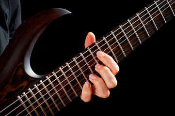 Seven-string electric guitar made of dark wood and human hands, shot on a dark background. Background for musical instruments and musicians.