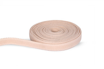 Rubber roll. Beige elastic band roll for sewing close-up. Fabric tape for needlework of the cloth on white background. Cloth ribbon made of polyester fibre for the production of knitwear textile tapes