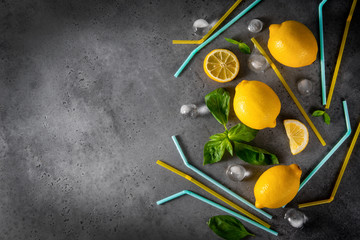 whole lemons, lemon slices, Basil, ice cubes, yellow and blue cocktail tubes on a gray background, top view