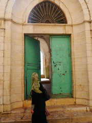single woman passing by open green door wearing green head scarf, Bethlehem