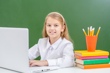 Smiling young girl uses laptop in a school