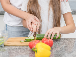Obraz na płótnie Canvas Closeup mom teaches her daughter to cut cucumbers for vegetable salad