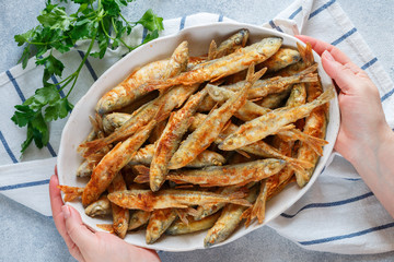 Fried smelt. A woman serves delicious small fish in a white plate. Gourmet appetizer. Selective focus, top view