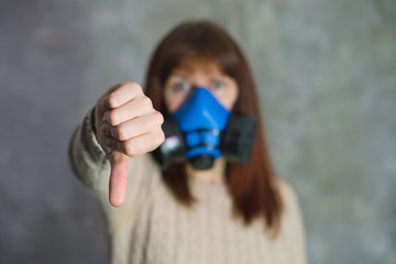 Girl in respirator shows thumb down on grey background. Isolation and virus protection concept.