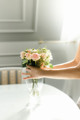 women's hands adjust a bouquet of roses on the table in the sun