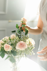 women's hands adjust a bouquet of roses on the table in the sun