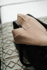 a beige sweater protrudes from a black travel bag on the bed