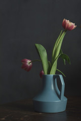 Blue vintage vase with pink tulips on wooden table.