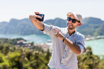 Handsome young man make video call on the phone enjoying the view in phi phi island view point. Summer vacations concept.