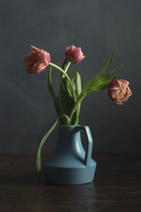 Vintage blue vase with pink tulips on wooden table.