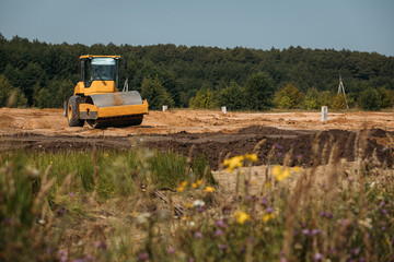 Obraz premium yellow asphalt paver compactor working on sand at a construction site