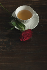 White china tea cup and saucer with red rose on wooden table. Top view.