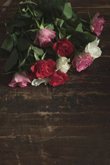 Red, pink and white roses left behind on wooden table.