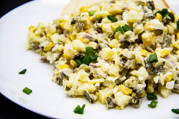 Ukrainian and Russian salad Olivier according to a new recipe on a white plate. Healthy salad Olivier with meat, corn and slices of white bread. Delicious and tasty salad on white plate.