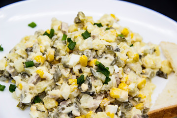Ukrainian and Russian salad Olivier according to a new recipe on a white plate. Healthy salad Olivier with meat, corn and slices of white bread. Delicious and tasty salad on white plate.