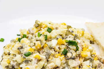 Ukrainian and Russian salad Olivier according to a new recipe on a white plate. Healthy salad Olivier with meat, corn and slices of white bread. Delicious and tasty salad on white plate.