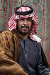 Portrait of Bedouin man wearing traditional headscarf sitting on a carpet in the Saudi desert