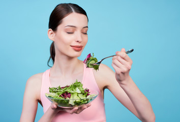 Cheerful fitness girl is eating vegetable salad.