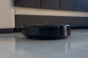 Robot vacuum cleaner automatically cleaning the floor. In the background, there is a couch.