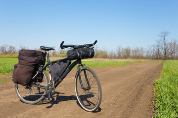 Obraz premium touristic travel bicycle with bags on a ground road among a fields