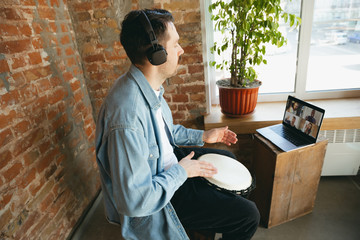 Caucasian musician playing hand drum during online concert at home isolated and quarantined. Using camera, laptop, streaming, recording courses. Concept of art, support, music, hobby, education.