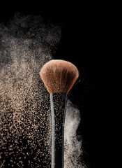 Natural bristle makeup brushes with splash of makeup powder on black background
