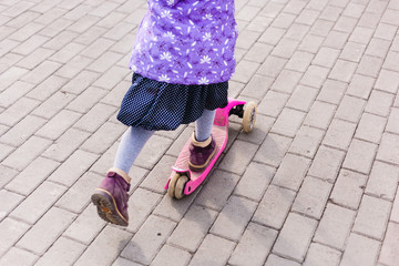 a girl in a hat and jacket rides a scooter, fun and movement, communication with other children,...