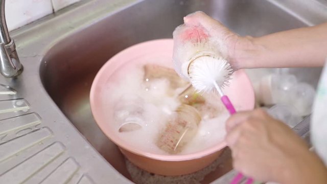 The baby bottle that is being used is being washed, the hands of the mother are cleaning the bottle by using plots and soap in the wash, the mother's leisure activity in the morning in child-rearing