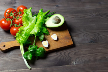 fresh vegetables, tomatos, avocado, salad leaves, basil, scallion, quail eggs on a wooden board on brown background