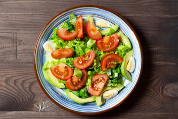 salad with tomatoes, green leaves, eggs, avocado in blue plate on brown wooden background