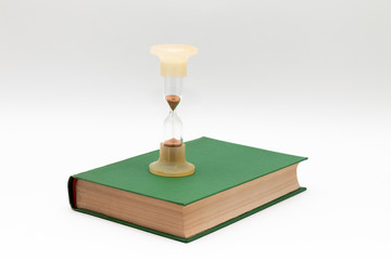 Hourglass on a green book. White background. Close-up.