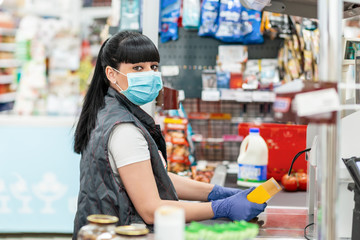 A young woman in a medical mask and gloves, working at the checkout in a supermarket. Concept of...