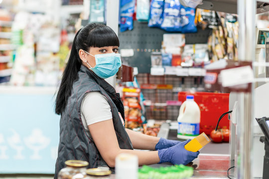 A young woman in a medical mask and gloves, working at the checkout in a supermarket. Concept of coronovirus, protection from infection and industrial crisis