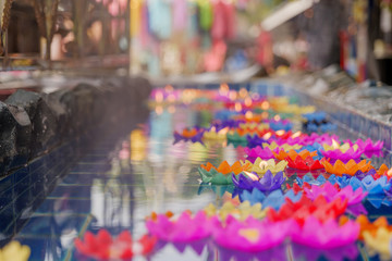 Close up view,  lotus flower candles with flame among floating colourful flower on water for worship buddha in Thai temple. Pray for buddha in traditional Asian culture. 