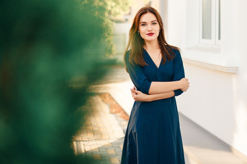 Red-haired model in a dark blue dress posing in the garden.