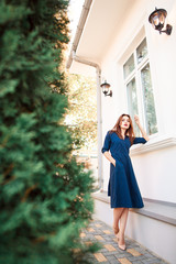 Red-haired model in a dark blue dress posing near the house