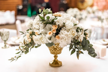 The bride's bouquet of white and yellow flowers on wedding arrangement in restaurant. Beautiful bridal bouquet of white and yellow peonies and roses on the table in the restaurant