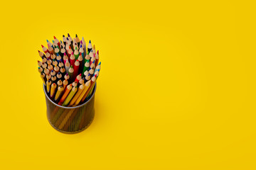 Colorful pencils in metal holder on yellow background. Education