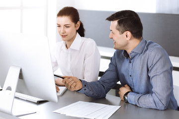 Cheerful smiling businessman and woman working with computer in modern office. Headshot at meeting or workplace. Teamwork, partnership and business concept