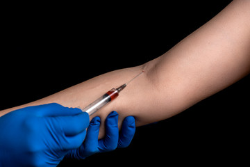 a doctor in disposable gloves takes blood from a patient’s vein for analysis on a black background