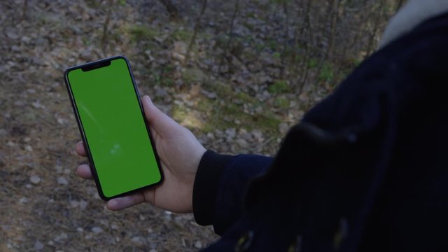 Hand tapping and swiping up on cell phone in the woods with chroma key green screen