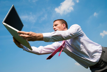 Stressed businessman reaching out to catch a laptop computer falling from blue sky