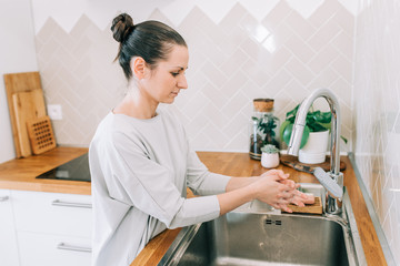 Hygiene to stop spreading coronavirus. Woman washing hands rubbing with soap in sink in kitchen.