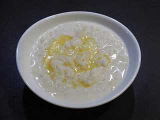 Milk rice porridge with butter in a white bowl closeup on a dark background, top view. Healthy grain pudding with cream for children for breakfast.