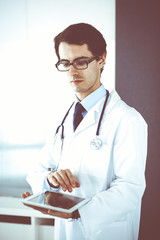 Fototapeta premium Doctor man using tablet computer for network research or virtual disease treatment. Perfect medical service in clinic. Modern medicine, medic data and healthcare concepts