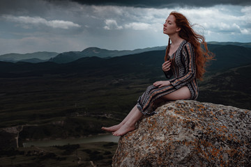 Ginger woman sits on a cliff and looks at an impending storm