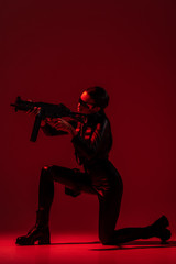 Fototapeta na wymiar futuristic african american woman in glasses aiming assault rifle on red background